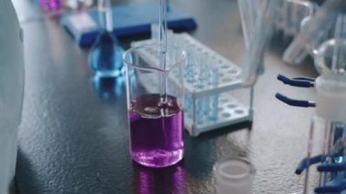 Laboratuvar teknisyeninin uzun cam pipetini mor kimyasal solüsyonla doldurup test yapmaya hazırlanırken yakın plan çekimleri.