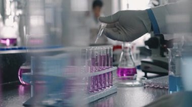 Eldivenli ve beyaz önlüklü isimsiz bir erkek kimyagerin pembe solüsyona pipetli test tüplerinde damlalar eklediği yakın çekim görüntüleri.