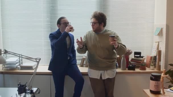 两个不同的白人男性办公室职员 穿着西服的完美主义者 穿着皱巴巴的休闲装的小丑 靠着窗台 喝咖啡 大笑的放大镜头 — 图库视频影像