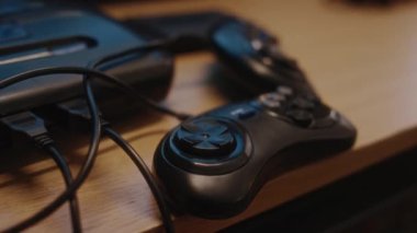 90 'lı yılların kapalı devre oyun konsolunun yanındaki masada eski oyun kumandasına el kamerasıyla bakan kimse yok.