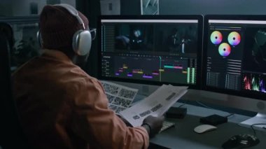 Stüdyo ofisinde oturan siyah erkek video editörünün orta arkası, film senaryosu ve senaryo danışmanlığı, profesyonel programda çekim sıralaması düzenlerken,