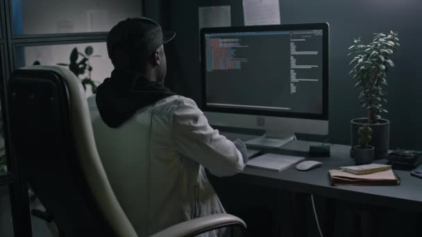 후드에 피곤한 아프리카계 미국인 프로그래머의 어두운 사무실에서 컴퓨터 코드에서 스트레칭 — 비디오