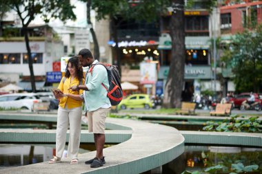 Bir çift genç gezgin şehir ortamında duruyor ve broşürde bilgi tartışıyor.