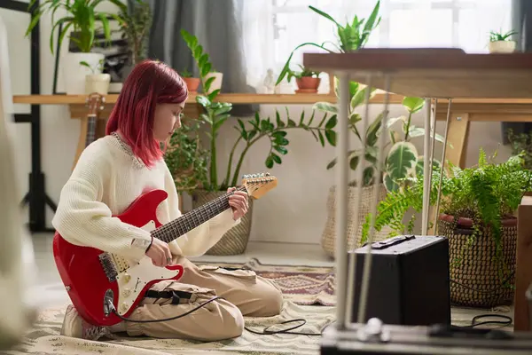 エレクトリックギターを演奏し 家庭のスタジオで新しい音楽を録音する若い女性のサイドビュー ストック写真