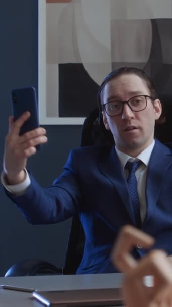 スーツのナルシシスティックな白人男性企業の上司 デスクに座っている眼鏡 プレイング スマートフォンでビデオ通話 いじめ 神経質な同僚を嘲笑 — ストック動画