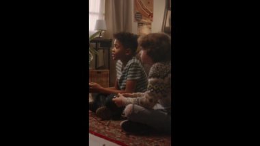 Halılı zeminde oturan ve nostaljik 90 'lı yılların atmosferi olan eski moda iç mekanlarda video oyununda geçen aşamalarda tezahürat yapan iki farklı arkadaşın el kamerasıyla çekilmiş dikey çekimleri.