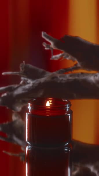 ドリフトウッド近くの赤いガラス瓶にアロマキャンドルを燃やして赤い抽象的なストライプの背景にロマンチックな雰囲気を生み出す垂直の人はいない — ストック動画