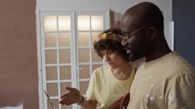 Kafkasyalı ve Afrikalı Amerikalı eşlerin bitmemiş odada dizüstü bilgisayar ekranına bakarak oda dekorasyonu fikirlerini tartışırken ve planlarken çekilmiş yan görüntüleri.