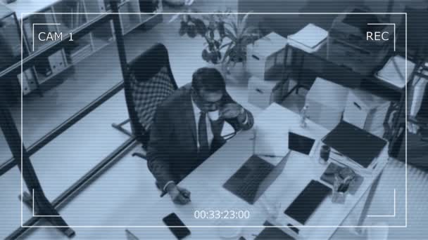 現代オフィスのテーブルでラップトップで作業しながらスーツやメガネを飲む上級男性のカメラ映像をトップビューCctvカメラ — ストック動画