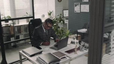 Modern hukuk firmasındaki bilgisayarlı belgeler ve kontratlarla çalışan gözlüklü ciddi bir çift ırklı avukatın uzun görüntüleri.
