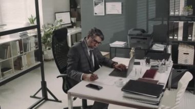 Çift ırklı erkek avukatın modern hukuk firmasındaki iş günlerinde dizüstü bilgisayarda çalışıp belgelere notlar aldığı görüntüler.