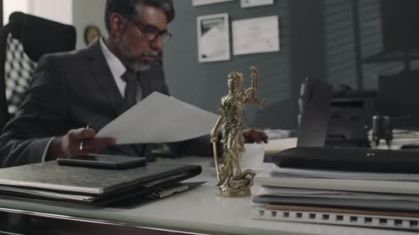 テーブルの上のレディ ジャスティスの青銅像に焦点を当てたサイド映像 バックグラウンドで論文を扱う上級弁護士 法律事務所 — ストック動画