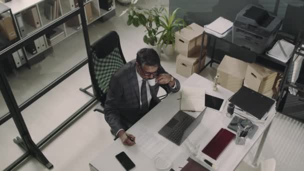 現代オフィスのテーブルでラップトップで作業しながらスーツとメガネを飲む上級男性の弁護士のトップビュー — ストック動画