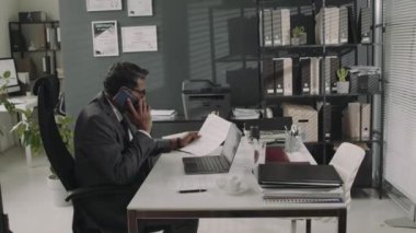 Takım elbiseli bir erkek avukatın telefon görüşmelerine cevap verirken ve avukatlık bürosundaki iş günlerinde doküman ve sözleşmelerden bahsederken tam görüntüler.