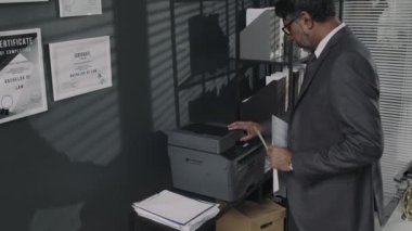 Takım elbiseli bir erkek avukatın modern ofisteki çok fonksiyonlu yazıcıyı kullanarak yasal belgeleri kopyaladığı ya da taradığı yan görüntüler.
