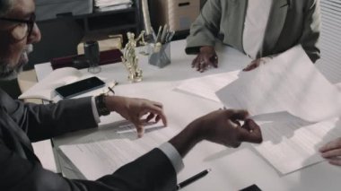 Çeşitli iş ortaklarının avukatlık bürosunda istişare sırasında ortak girişim anlaşmasının kopyalarını imzalamalarının yan görüntüleri.