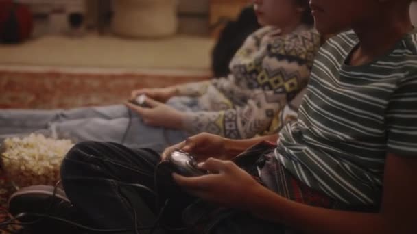テレビコンソールのビデオゲームを失った多様な子供たちのサイドチルトハンドヘルド映像と 暖かいリビングルームの床に座っている間に動揺を見ている90年代の大気ケアフリーの子供時代 — ストック動画