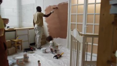 Gelecekte küçük kızıyla birlikte duvar boyayan yorgun kocaya kahve getiren hamile beyaz kadının tam görüntüsü.