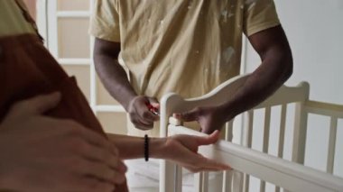 Kafkasyalı hamile kadının Afrikalı Amerikalı kocasına doğmamış bebekleri için beşiği bağlamasına yardım ederken çekilmiş yan görüntüler.