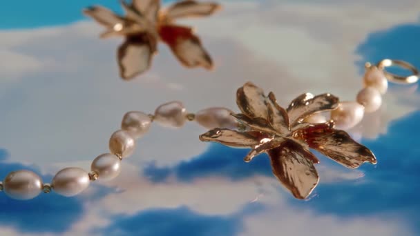 スタジオの抽象的な白と青の背景に真珠のブレスレットによって横たわるエレガントなヴィンテージの黄金の花のイヤリングの広告のマクロのクローズアップはありません — ストック動画