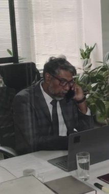 Tecrübeli bir çift ırklı avukatın ofiste yasal belgeler hazırlamak için müşteriyle telefon görüşmesi yaparken çekilmiş dikey görüntüler.