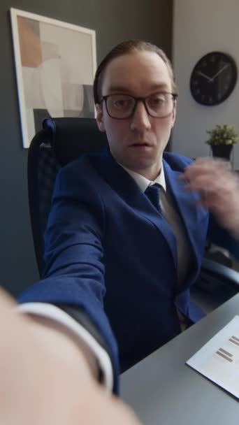 白种人男性职员坐在办公桌前 拿起智能手机 剪短发 拉直眼镜 拍摄演示文稿时的中等垂直自拍 — 图库视频影像