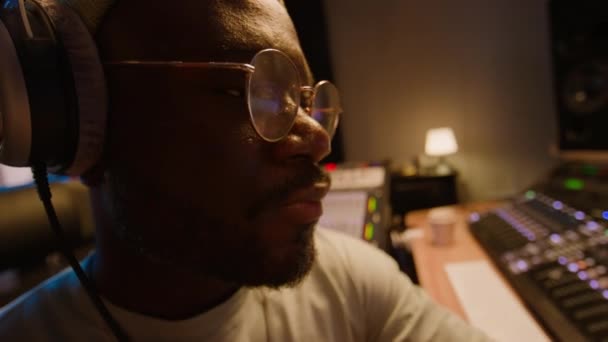 集中的非洲裔美国人音乐制作人或Dj坐在录音室里 在耳机里听音乐 欣赏音乐效果 摇头以达到节拍 — 图库视频影像