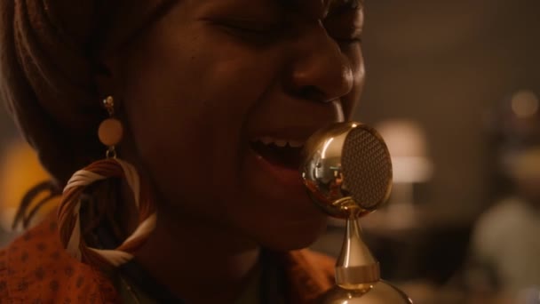 戴头巾的非洲裔美国人乐队歌手的特写 戴着大耳环进行情感表演 对着金色老式话筒唱歌 在俱乐部和乐队一起演奏 — 图库视频影像