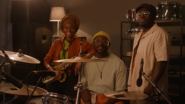 ハッピースタイリッシュなアフリカ系アメリカ人の男性と女性のバンドメイトのミディアムフルポートレート レコーディングスタジオでドラムキットの周りに立って カメラを見て笑顔 — ストック動画