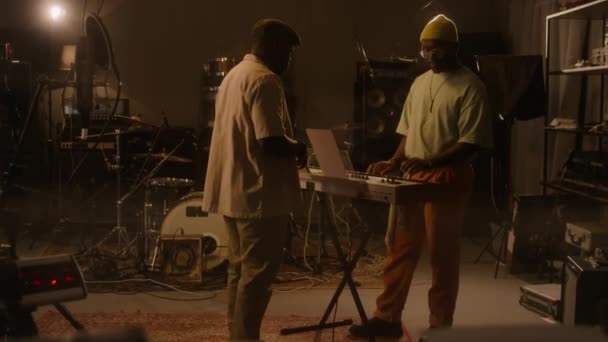 レコーディングスタジオのキーボードに立っているアフリカ系アメリカ人男性ミュージシャン コードを演奏 新しい音楽素材に取り組み サクソフォンが歩いて参加する女性バンドメイト — ストック動画