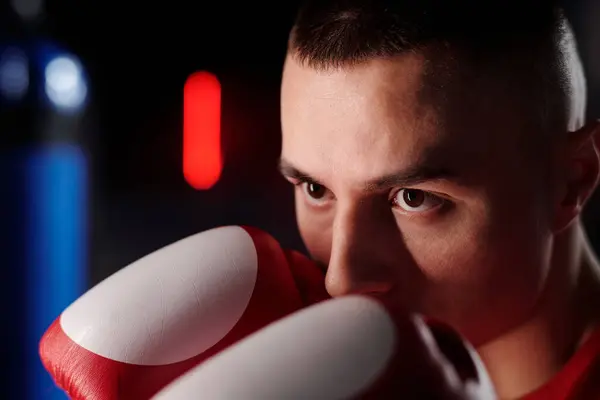 若い男性ボクサーの顔は パンチバッグの前に立っている間 鼻でボクシング手袋に手を保ちます ロイヤリティフリーのストック写真