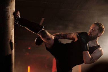 Genç sakallı erkek boksörün kollarında ve göğsünde dövmeleri var. Düşük tekme ve diğer temel boks teknikleri uyguluyorlar.