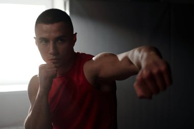 Yumruklarını sıkmış genç ve ciddi bir adam temel tekmeler ve savunma teknikleri üzerinde çalışırken rakip veya kum torbasına konsantre oluyor.