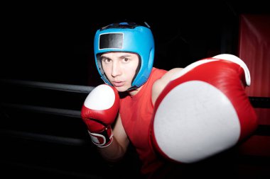 Genç erkek boksör boks eldiveni içinde sol eliyle rakibini dövüyor ve boks ringinde dövüşürken sağ eliyle defansı koruyor.