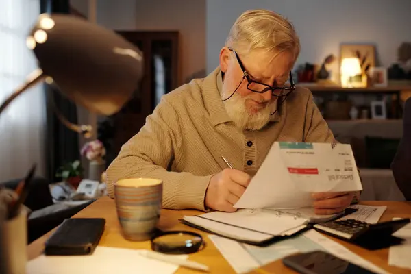 Pria Senior Dengan Tagihan Listrik Tangan Membuat Catatan Notepad Sambil Stok Foto Bebas Royalti
