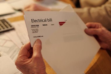 Masanın başında oturup ödeme belgelerini kontrol ederken beyaz zarftan katlanmış elektrik faturasını alan tanınmamış yaşlı bir kadının eli.