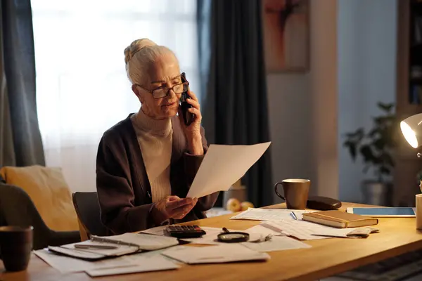 Donna Anziana Difficoltà Con Telefono Cellulare Orecchio Guardando Documento Cartaceo Foto Stock