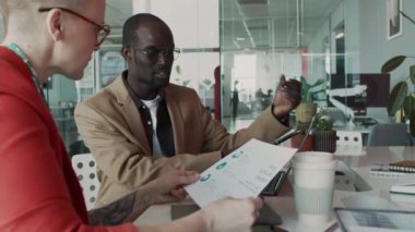 Gözlüklü Afrikalı Amerikalı bir adamın ofis toplantısı sırasında beyaz kadın meslektaşıyla konuşması iş sunumunu tartışırken yeni bir reklam stratejisi öneriyor.