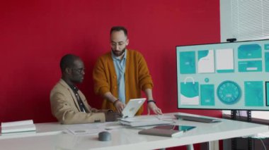 Afrika kökenli Amerikalı ve Orta Doğulu erkek meslektaşların toplantı odasında konuşurken, tabletteki ürün tasarımına bakarken, bunu tartışırken, kırtasiye şablonuyla dijital ekranın yanında.