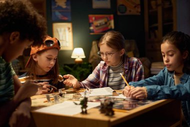 Gündelik kıyafet giyen birkaç kültürler arası çocuk yeni masa üstü oyununun kurallarını okuyor ve birlikte oynamadan önce karakter rollerini seçiyorlar.