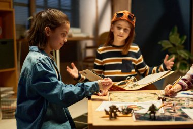 Kot ceketli genç bir kızın masa başında yeni bir masa oyunu oynarken zar atması ve arkadaşlarıyla oynaması.