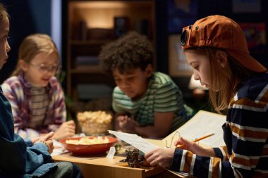 Beyzbol şapkalı ve çizgili kazaklı yakışıklı çocuk arkadaşlarının arasında otururken yeni masa başı oyununun rol ve karakterlerini inceliyor.