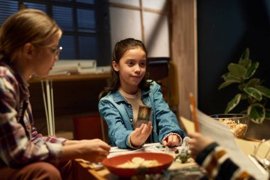 Arkadaşları arasında oyun tahtası ve heykelciklerle masada otururken bir grup oyuncuya kartını gösteren sevimli genç kız.