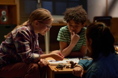 Bir grup kültürlü kültürlü genç kız masa başında masa başında oyun oynarken gözlüklü kız zar atıyor.