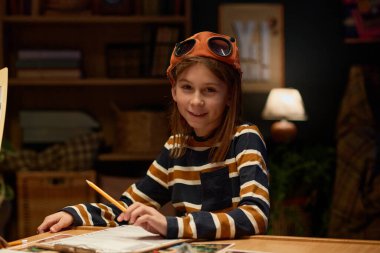 Çizgili uzun kollu kazak ve kahverengi beyzbol şapkalı mutlu gencin portresi masa oyunu kurallarını okurken kameraya bakıyor.