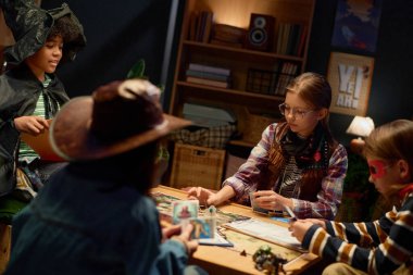 Masanın başında oturup oyun oynarken karakter figürünü veya oyun tahtasının diğer parçasını hareket ettiren dört kültürler arası gençlik arkadaşından biri.