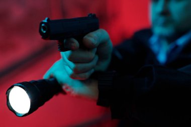 Profesyonel güvenlik görevlisinin parmağı silah tetikte ve karanlık koridoru el feneriyle aydınlatıyor.