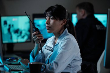 Gözetim odasındaki genç, ciddi İspanyol bayan memur bilgisayar ekranına bakarken telsizle durumu bildiriyor.