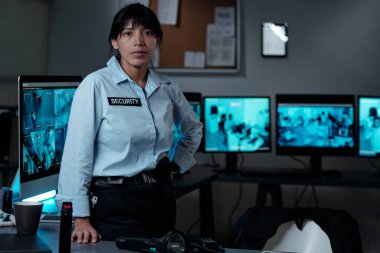 Ciddi ciddi İspanyol üniformalı kadın güvenlik görevlisi gözetleme odasında kapalı devre televizyon sistemiyle sana bakıyor.