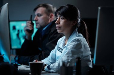 Gözetim bölümünden genç ve ciddi bir bayan memur olgun bir erkek arkadaşa karşı bilgisayarın ekranına bakıyor.